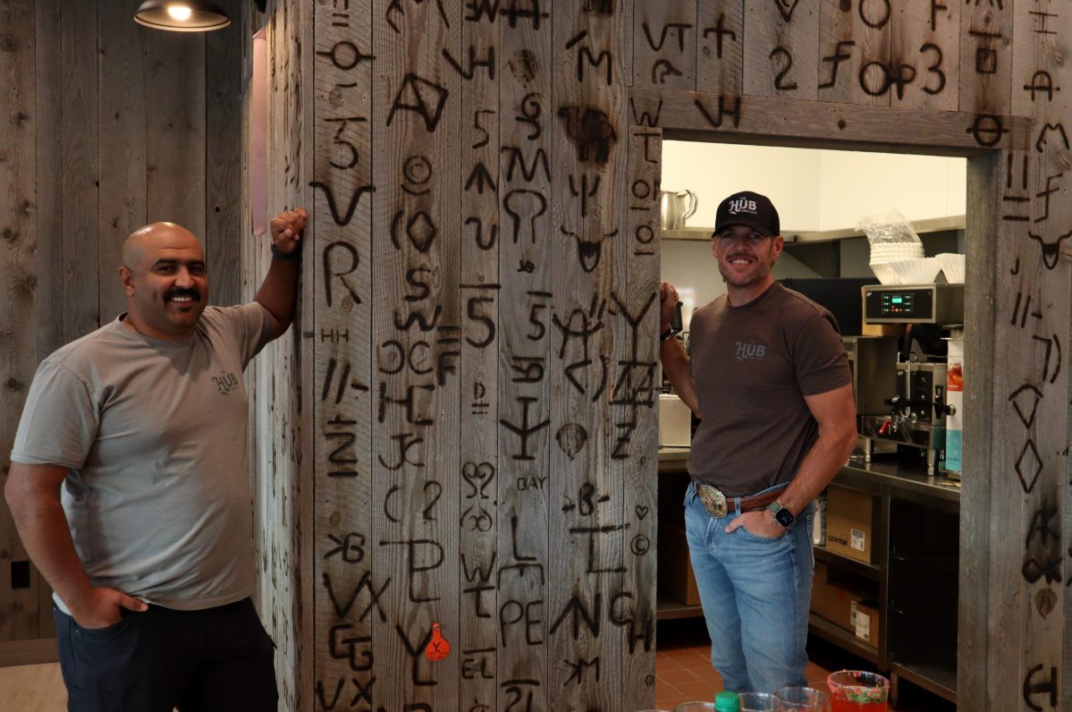 The Hub co-owners Mohamed Mohamed and Devin Johnson stand next to their restaurant's branded wall.