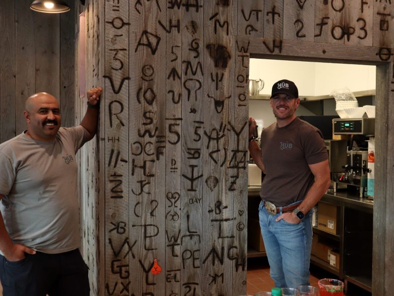 The Hub co-owners Mohamed Mohamed and Devin Johnson stand next to their restaurant's branded wall.